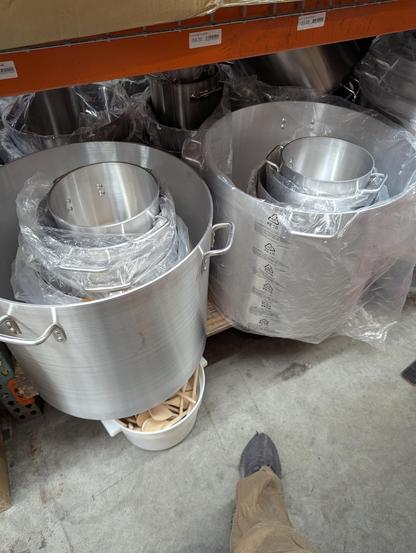 A foot next to some giant aluminum pots with four handles the pots were probably over two feet tall