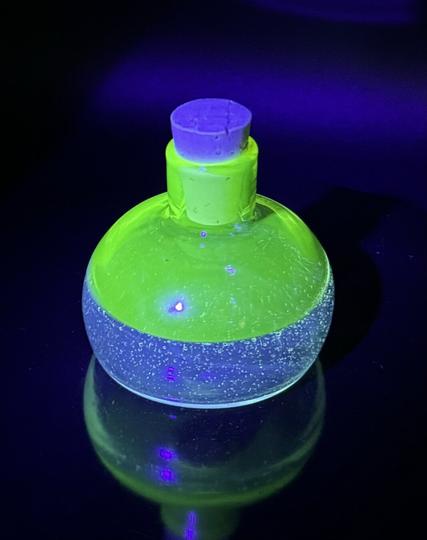 Uv reactive glass bottle with cork, top part glows green and bottle part glows blue.