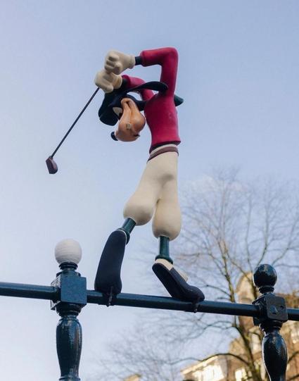 Streetart. The artist "Frankey" has created a fun installation on a metal bridge railing on the canal in Amsterdam. The black metal fence is decorated with small black balls on the railing. Between two of these balls, the artist has placed a self-designed, standing and large Goofy figure in a golfer's outfit. Goofy, the long Walt Disney dog with floppy ears, is swinging his golf club to hit one of the balls. This has been painted white and now really does look like a golf ball. Very funny and hopefully no one will steal it within 20 minutes.
Info: Frankey is Frank de Ruwe who
currently lives and works in Amsterdam. Where, if you look closely, you can discover his works in an unexpected places throughout the city. Frankey manages to give passers-by an instant smile from ear to ear time after time. "Pretty cool, right?", He says himself.