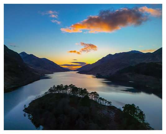 Sunset over the Lochaber Hills in the Western Highlands. In the foreground an island covered in Scots Pine trees, with snow dusted peaks in the distance.