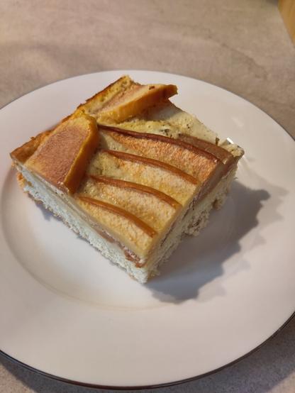 ein Stück des Quittenkuchen auf einem weißen Kuchenteller. die Quittenspalten wurden lamellenartig auf dem Teig und dem Guss angeordnet, was auch gebacken sehr hübsch aussieht.