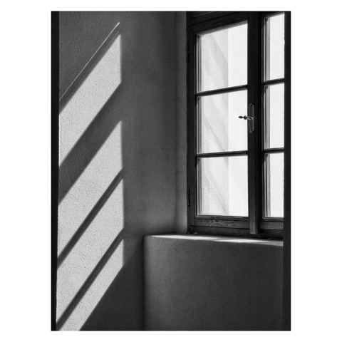 This is a high contrast black and white image in portrait format. It depicts light falling through a window. The window occupies the top two thirds of the right hand side of the image. Diagonal patches of light and shadows dominate the left. Taken in Prague.