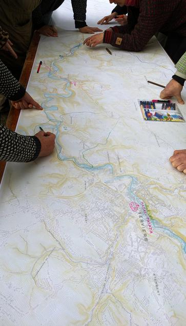 Photo d'une impression large d'une carte de la vallée de la Vesdre sur laquelle des participant.es annotent des lieux aux marqueurs colorés.