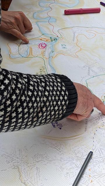 Photo d'une impression large d'une carte de la vallée de la Vesdre sur laquelle des participant.es annotent des lieux aux marqueurs colorés et un participant pointe du doigt un lieu particulier.