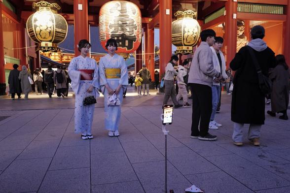 Zwei Frauen in traditionellen Kimonos posieren vor einem Tempel mit großen roten Laternen. Ein Smartphone auf einem Stativ steht vor ihnen, während im Hintergrund andere Menschen die Szene beleben. (Tokyo, Dembo-in Tempel)