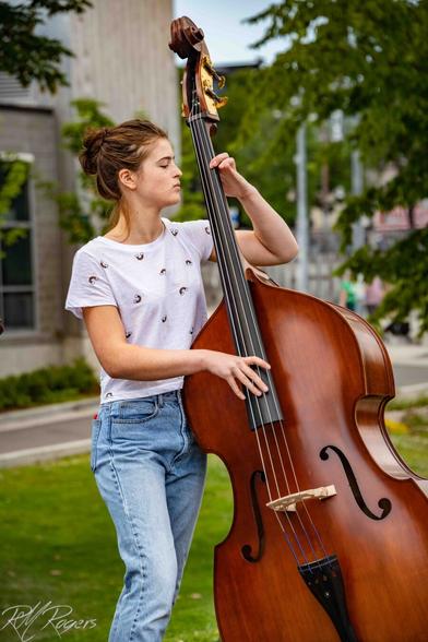 A woman plays the bass fiddle in a park.