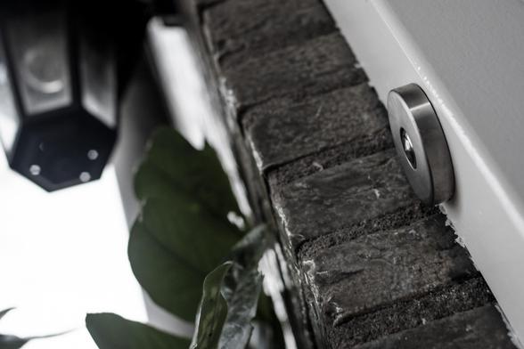 Photo from a low perspective of a doorpost and door bell, with in the background an outdoor lamp. In the left corner a few dark green leaves.