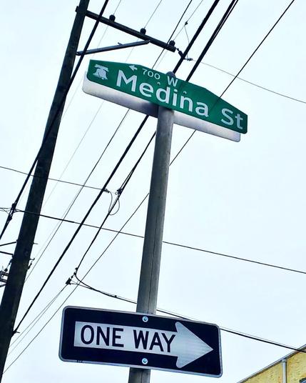 Photo of a street sign, taken from below, for Medina Street in South Philadelphia. Below the strewt sign is a one way sign. The arrow points to the right. Telephone lines are strung between poles above the signs.