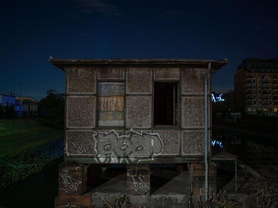 ein altes Haus mit zugenageltem Fenster am Flussufer bei Nacht