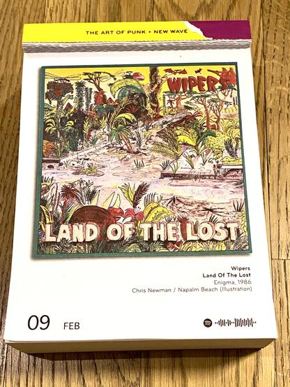 Das Bild zeigt ein farbenfrohes, handgezeichnetes Cover eines Albums mit dem Titel “Land of the Lost” von der Band Wipers.

Es stellt eine üppige, wilde Landschaft dar, die an eine prähistorische oder post-apokalyptische Welt erinnert. Die Szenerie ist voller exotischer Pflanzen, Palmen und dichter Vegetation. Inmitten der Landschaft befinden sich verschiedene prähistorische Kreaturen, darunter Dinosaurier und riesige Echsen. Im Vordergrund liegt ein großes gehörntes Tier mit braunem Panzer, das an einen Triceratops erinnert. Außerdem sind verstreute Knochen zu sehen, die auf eine lebensfeindliche Umgebung hinweisen.

Der Himmel ist gelb-orange gefärbt, und im oberen Bereich fliegen Fledermäuse oder urzeitliche Flugsaurier. Der Schriftzug “WIPERS” ist groß, rot und kantig gestaltet, während “LAND OF THE LOST” in massiven, weißen Buchstaben mit einem erdigen Farbverlauf am unteren Rand prangt.

Die gesamte Gestaltung hat einen handgezeichneten, fast psychedelischen Stil mit kräftigen Farben und wilden Details, die eine surreale, abenteuerliche Stimmung erzeugen.