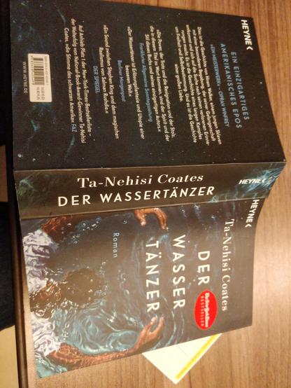 Das Buch Der Wassertänzer von Ta-Nehisi Coates liegt aufgeschlagen, mit der Außenseite oben, auf einem Tisch.