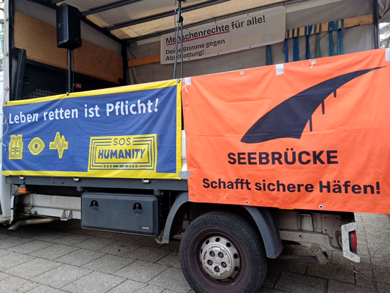 Am Lauststrecherwagen hängen Transparente mit Parolen: "Menschenrechte für alle! Deine Stimme gegen Abschottung", Leben retten ist Pflicht! (SOS Humanity)" und "Seebrücke: Schafft sichere Häfen!"