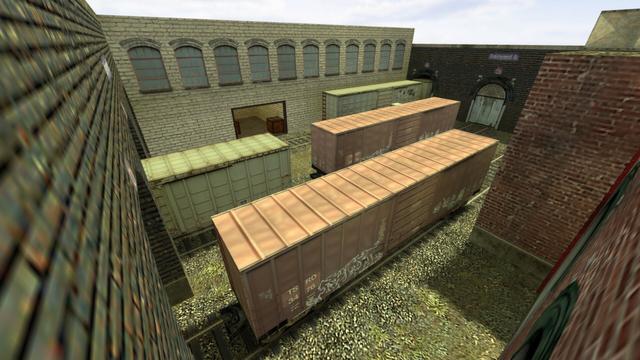 In this picture you can see the Trainyard B from diagonally above. Unlike Trainyard A, it has no roof. You can see a total of five container wagons standing on three rails. Of these, three are white and two red. Again, the colors have faded from the wagons. In the background you can see an entrance towards Trainyard A. On the right edge you can still see a red ladder on a building. This is on the map de_train in the game Counter-Strike 1.6.