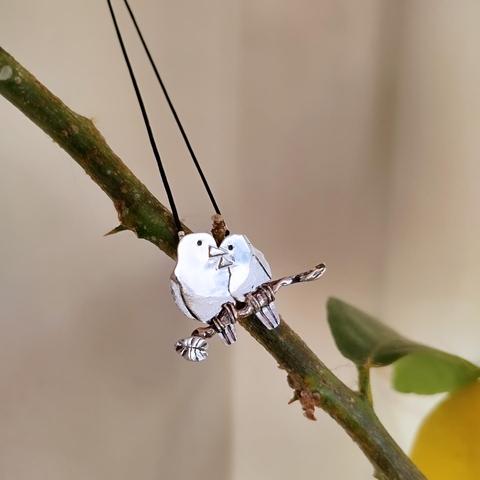 A silver pendant with two loving birds. it has a black cord.