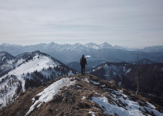 centered back view of a person walking along a ridge with snowy peaks in the distant