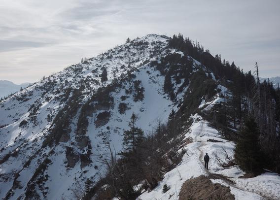 a path meanders up a slope with a peak and a tiny cross visible in the background