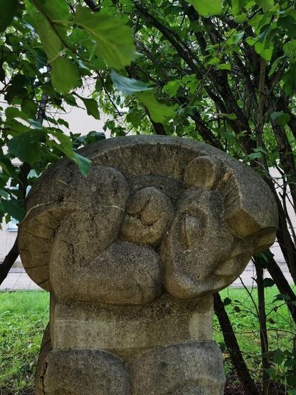 Rock sculpture of a sleeping hedgehog hidden in green bushes.