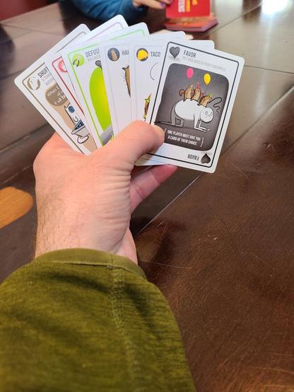 Picture of hand above a table holding hand of cards from the card game Exploding Kittens.