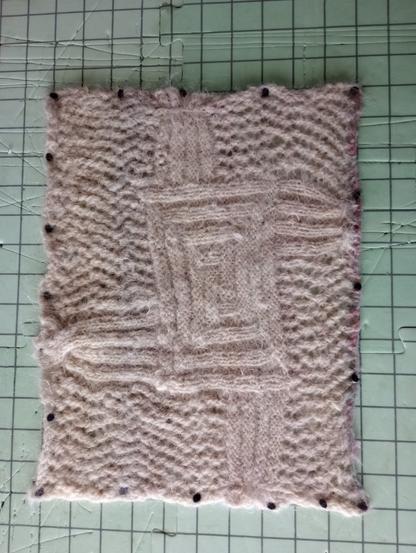 A square of hand knitted fabric depicting the Brigid's Cross symbol