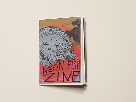 Cover of a mini-zine. It contains a cut out flounder drawn in black ink on white paper glued to a colourful background with mainly pink, orange yellow colours.