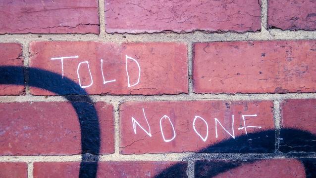 Close-up of a brick wall with graffiti reading "TOLD NO ONE" in thin white letters.