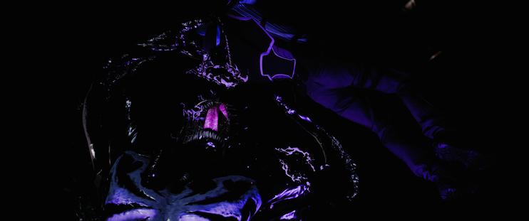 Dimly lit, Venom is holding a man up with both arms, seemingly either about to bite him or tear him in two pieces