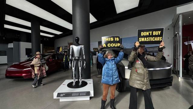 Demonstrators inside a Tesla showroom hold signs reading "This is a coup" and "Don't buy swasticars."