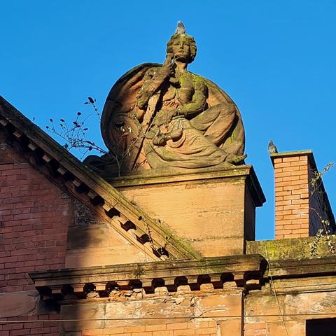 A sculpture of a winged female figure kneeling while holdibg a sword and scales.