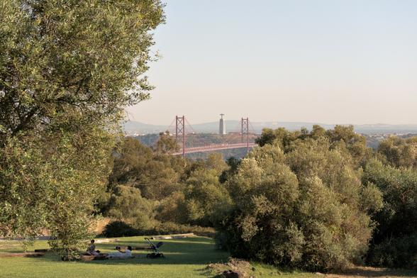View of the 25 de Abril bridge, and the Cristo Rei Statue, as seen from Monsanto. Upfront a few people strolling around Monsanto.