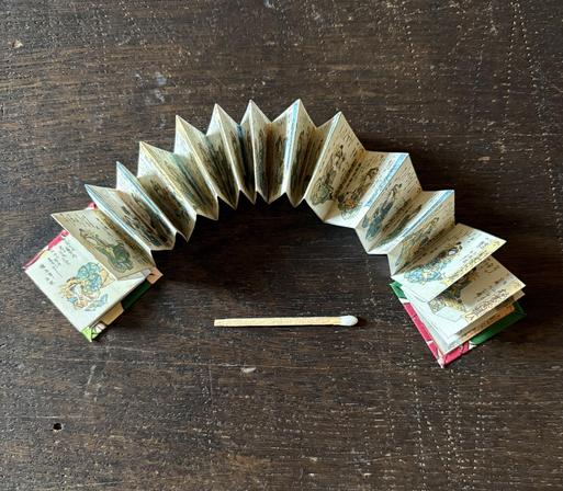 An open, accordion miniature book with illustrated pages is displayed on the table.