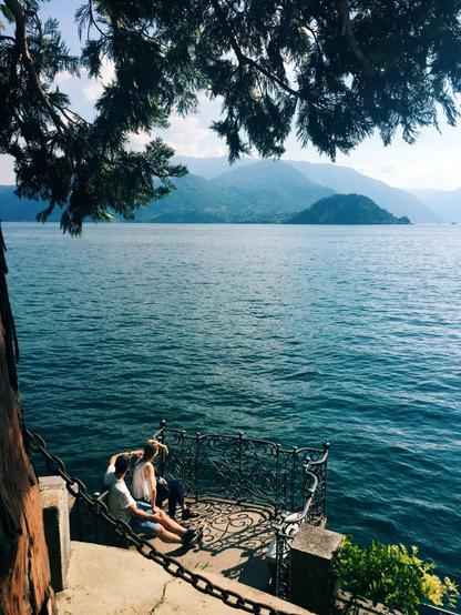 a photo of a couple sitting on a bench in the public gardens of Villa Monastero in Varenna, looking out at Lake Como