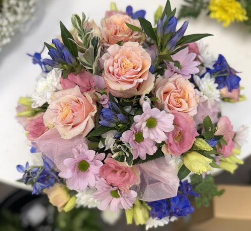 An all round posy arrangement in shades of peach, blue, cream and pale pink. The flowers used were roses, chrysanthemum, gentian, deliphium and lisianthus with a mix of eucalyptus, pistache and euonymous foliages.