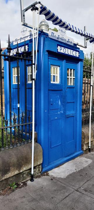 Sininen Police Box seisoo rautaisen aidan keskellä jalkakäytävän vieressä.
