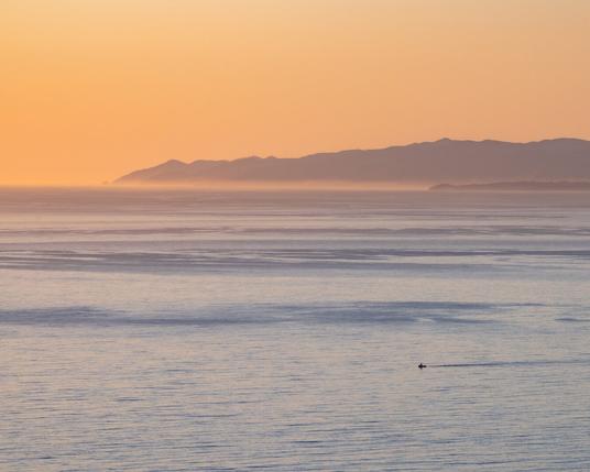a sunset photo of mine shot at Palos Verde California, the sky has clouds in a yellow and pink tones over seen a beach with a boat going across the ocean.