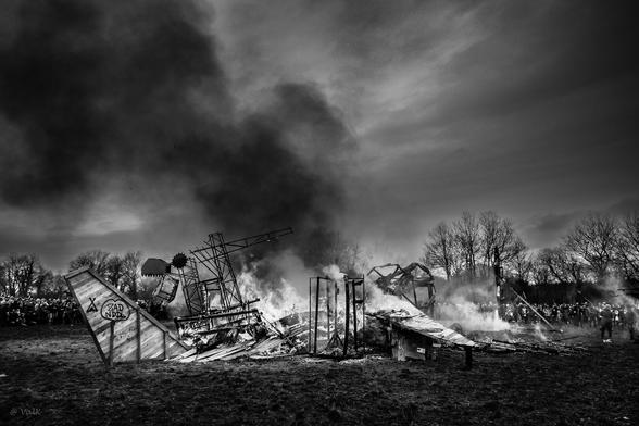 photo en noir et blanc très contrastée où on voit une carcasse d'avion en bois et métal terminer de bruler. Sur un morceau de la queue encore intacte on peur voir un ZAD NDDL tagué dans un coeur. On devine une grande foule en cercle tout autour.