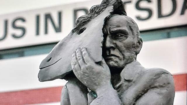 Graue Skulptur vor dem Museum in Potsdam stehend, Mann hält einen Pferdekopf wie eine Maske seitlich an seinen kopf