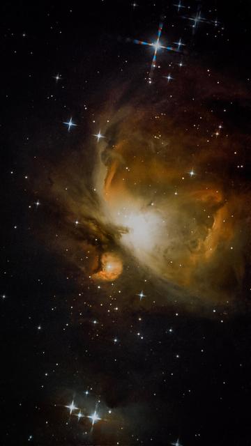 A vibrant image of a nebula in space, featuring swirling clouds of gas and dust illuminated by stars. The background is dotted with numerous bright stars against a dark backdrop, showcasing cosmic beauty.