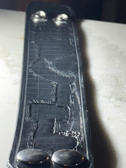 A low angle photo showing a textured relief dungeon map in the old school crosshatch style, but carved into a leather bracelet/cuff