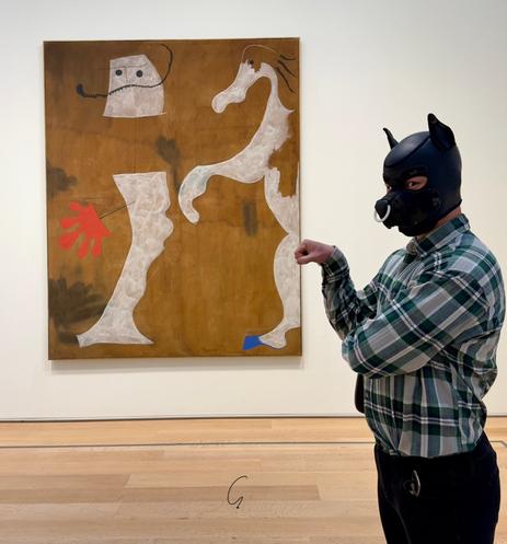 A playful juxtaposition of surrealism and kink unfolds in this image. A person wearing a black/camo neoprene puppy hood, a staple in the pup play culture, strikes a whimsical pose beside Joan Miró's 1925 painting “The Policeman.” The artwork, housed at the Art Institute of Chicago, features biomorphic shapes representing a policeman and a horse, rendered in Miró's signature dreamlike style. The person mimics the dynamic energy of the painting, extending their fist as if playfully interacting with the abstract forms.

The scene blends the avant-garde surrealism of Miró with the contemporary fetish subculture, creating an engaging commentary on identity, role-play, and artistic expression. The museum setting adds an extra layer of irony, as the human "pup" brings a tactile, performative dimension to the otherwise static art piece.