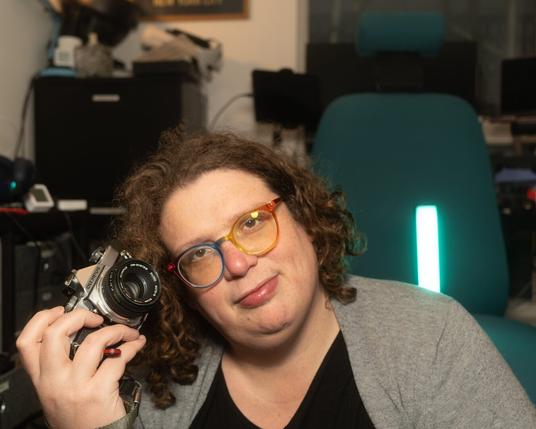 Gemma wearing rainbow glasses and holding an olympus OM1 in her right hand.