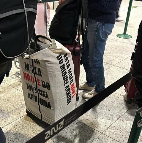 Photo of a line at a Portuguese airport featuring a suitcase wrapped up in a bag that states, in Portuguese, "this suitcase doesn't belong to Miguel Arruda". Context: Miguel Arruda is a Portuguese far-right MP that has been detained and accused of stealing suitcases at airports.