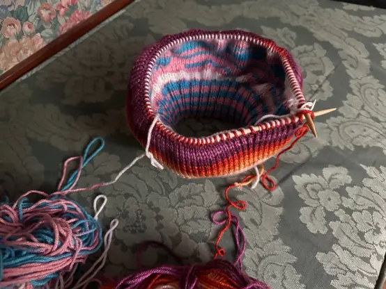 a view of my reversible trans/lesbian pride tam from above, angled so that the inside of the doubleknit fabric can be seen somewhat.  parts of both extrodinarily messy skeins of yarn are visible in the lower left corner of the image