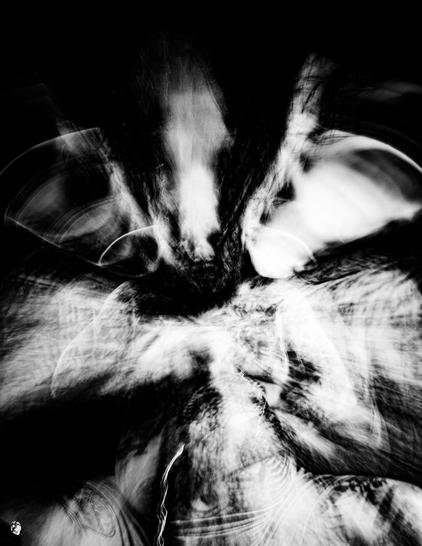 Black and white low key photo, Blurry silhouette with pig's ears extruded towards the outside, the impression is nightmarish, the person cannot be recognized, seems to grow out of the picture, to expand. Black sun with shadowy body shapes, the head distorted like a long animal skull.