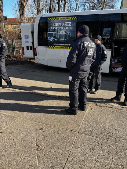 Poilizisten vor Bus mit Aufschrift "Adenauer SRP+ Ersatzverkehr".