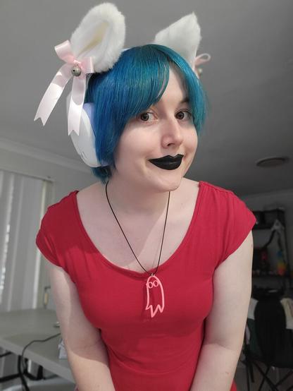 Selfie of Revy wearing black lipstick and purple and white headphones with white pink fluffy cat ears attached and a I saw the tv glow link opaque necklace.
And a cute red dress
She has short blue hair