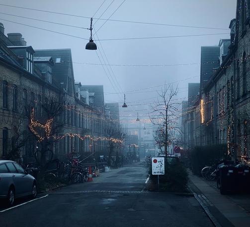 Dark moody street with lights hanging everywhere. Moody and foggy with a monolithic building seen slightly in the distance.