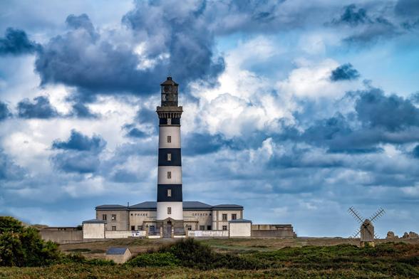 The image depicts a lighthouse with alternating black and white stripes. It is labeled "Phare de Créac’h." The lighthouse sits on a grassy landscape under a cloudy sky. To the right, there is a windmill.