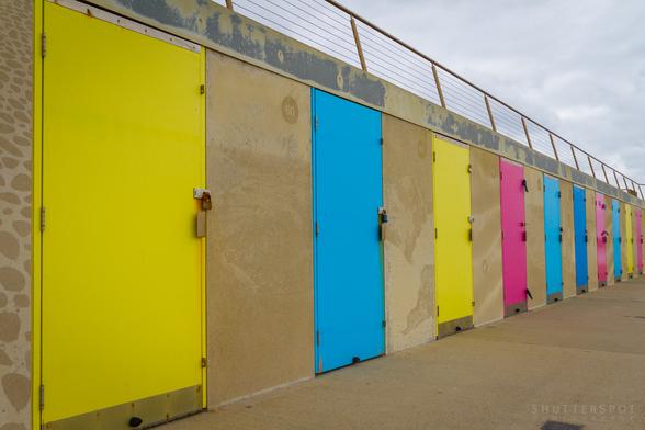 Picture shows a row of beach chalet doors in bright colours of yellow, blue and pink.