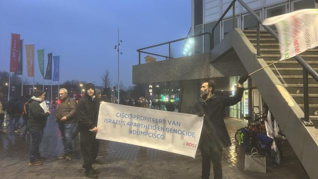 Two people holding banner saying "Cisco profits off israeli apartheid and genocide. #Dumpcisco "