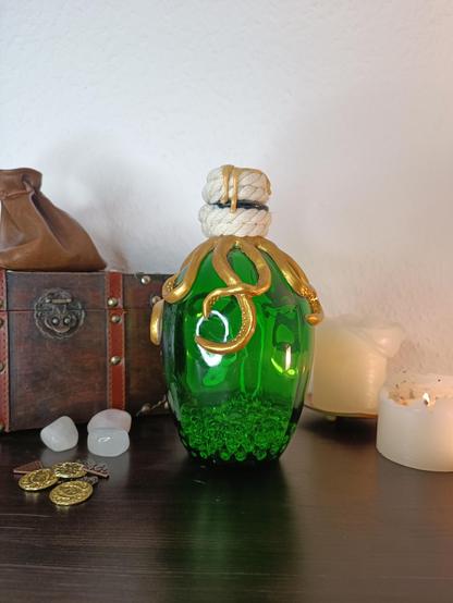 A green bottle is standing on a table. The arms of a golden octopus  are twisted around the neck and body of the bottle.